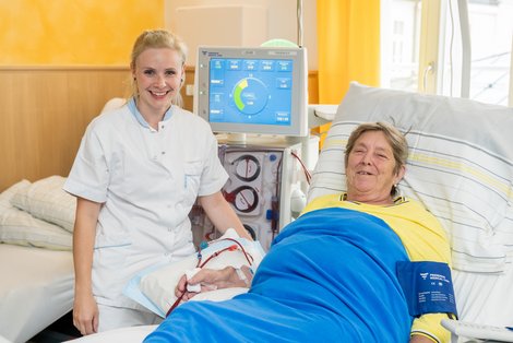 Patientin im Bett bei der Dialyse, an ihrem Bett steht Krankenpflegerin