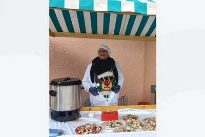 Mitarbeiterin verkauft in Weihnachtspulli und mit Zipfelmütze Kekse und Punsch