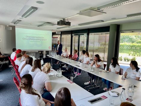 Auszubildende sitzen an langem Tisch und schauen Präsentation an.