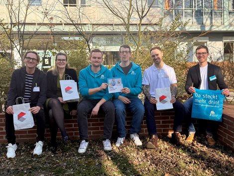 Mehrere Personen sitzen mit Infomaterial in der Hand auf einer Mauer