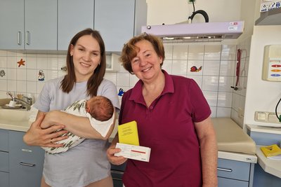 Mama mit Baby im Arm und daneben die Ärztin mit Impfpass und Impfstoff