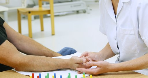 Mitarbeiterin der Ergotherapie trainiert mit Patient die Hand 