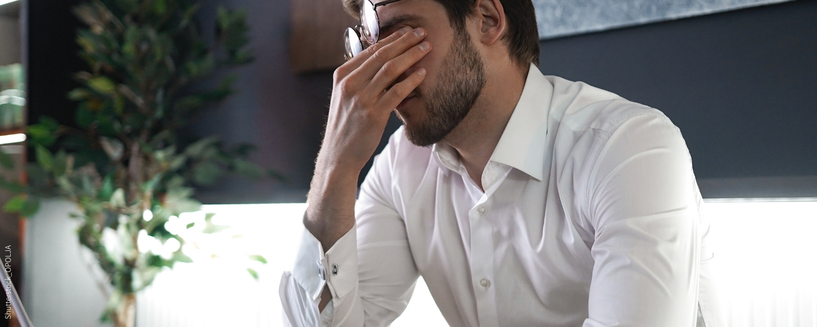 Mann in einem Büro schiebt Brille hoch und reibt sich die Augen