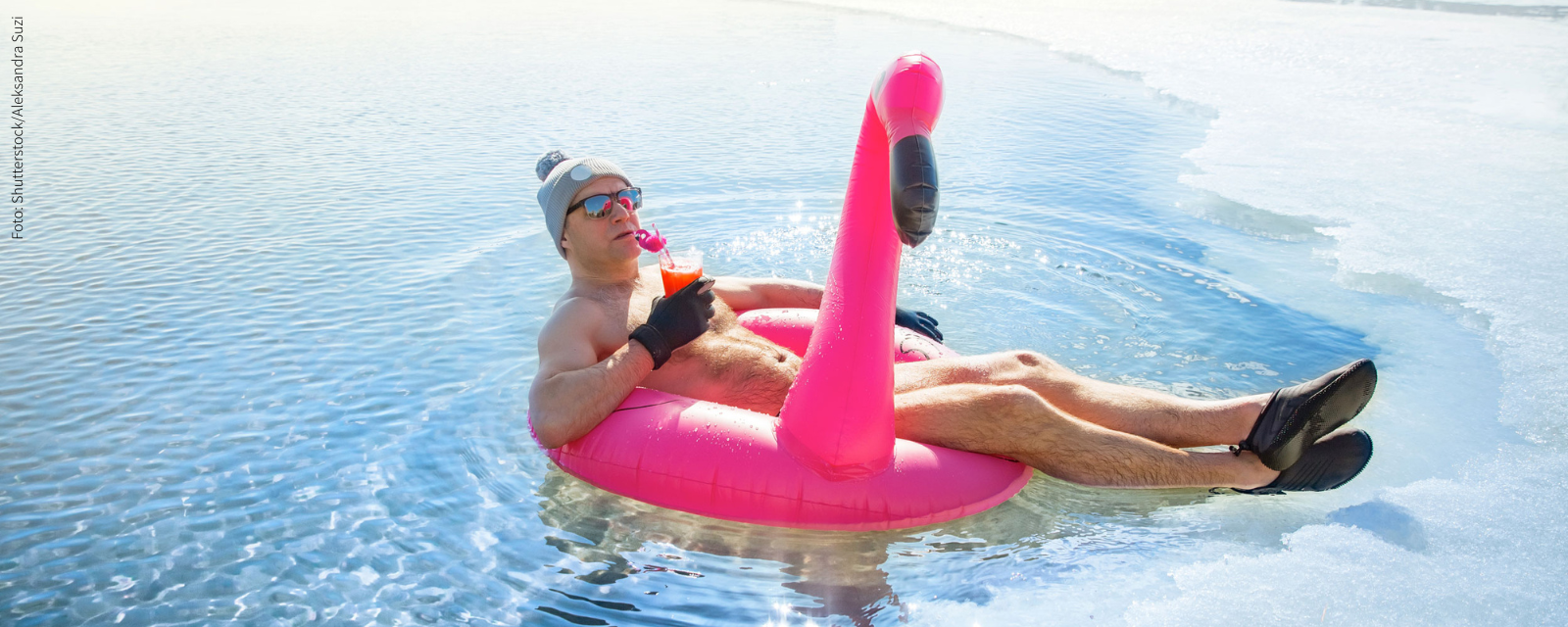 Mann beim Eisbaden auf Flamingo-Luftring mit Cocktail und Sonnenbrille